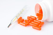 Orange pills and thermometer on white background