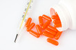 Orange pills and thermometer on white background