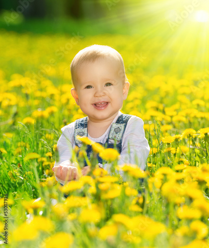 Photo: happy baby girl on meadow with yellow flowers on the nature happy baby girl on meadow with yellow flowers on the nature