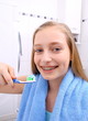 Blond girl with braces smiling while brushing your teeth