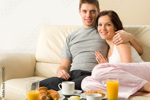 Photo: Cheerful couple sitting on couch before breakfast Cheerful couple sitting on couch before breakfast