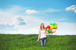 Happy young woman with colorful balloons on a green meadow
