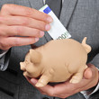 man in suit introducing a euro bill in a piggy bank