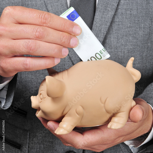 Photo: man in suit introducing a euro bill in a piggy bank man in suit introducing a euro bill in a piggy bank