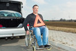 Man in a wheelchair and warning triangle next to his car