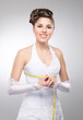 A young and beautiful bride measures her waist over the grey