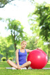 Young female in sportswear sitting on a grass with fitness ball