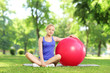 Young female in sportswear sitting on a grass with pilates ball