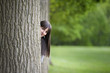 young woman hiding behind a tree