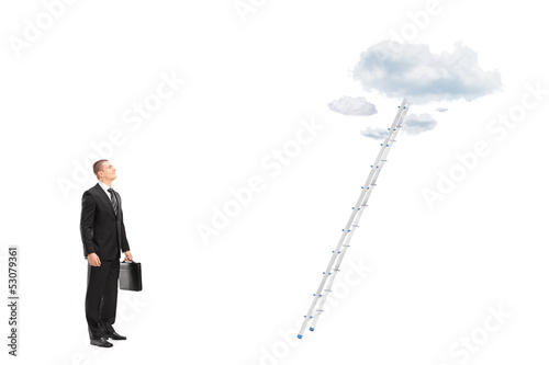 Photo: Businessman standing in front of a ladder with clouds looking up Businessman standing in front of a ladder with clouds looking up