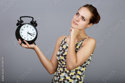 Photo: Thoughtful girl with alarm clocks at gray background Thoughtful girl with alarm clocks at gray background