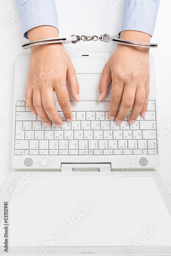 Photo: Female hands in handcuffs, with laptop, high angle view Female hands in handcuffs, with laptop, high angle view