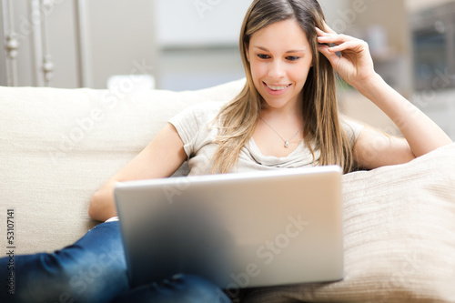 Photo: Woman using a laptop while relaxing on the sofa Woman using a laptop while relaxing on the sofa
