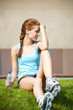 Woman skating in city. Girl going rollerblading sitting in grass