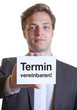 Junger Mann im Anzug mit Karte TERMIN VEREINBAREN!