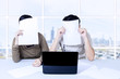 Couple hiding behind papers sitting with laptop