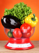 Photo: Fresh vegetables in scales on table on orange background Fresh vegetables in scales on table on orange background