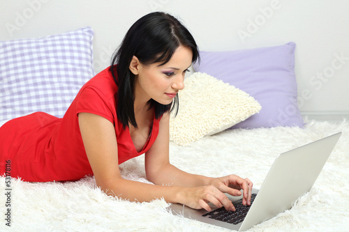 Photo: Beautiful young woman lies with notebook in room Beautiful young woman lies with notebook in room