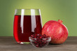 Glass of fresh garnet juice on table on green background