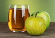 Glass of fresh apple juice on table on green background