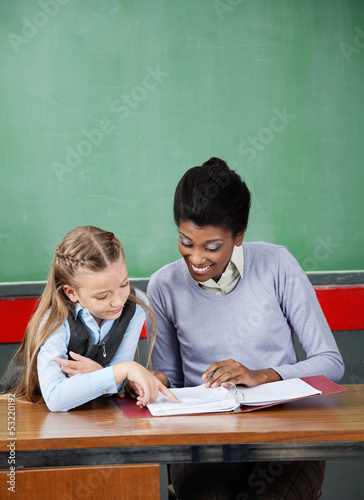 Photo: Schoolgirl Pointing In Binder With Teacher At Desk Schoolgirl Pointing In Binder With Teacher At Desk