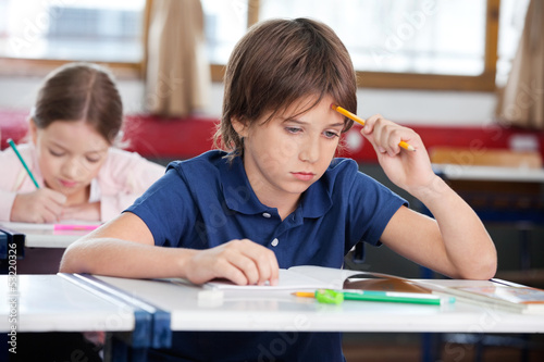 Photo: Thoughtful Schoolboy Sitting At Desk Thoughtful Schoolboy Sitting At Desk