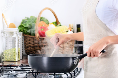 Photo: Woman standing by stove cooking and preparing meal Woman standing by stove cooking and preparing meal