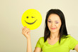 Young woman holding paper with happy smiley on gray background.