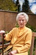 Happy oldere woman with a walking stick sitting outdoors