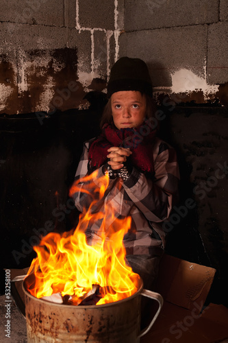 Photo: Poor beggar child warming up at the fire in a tin pot Poor beggar child warming up at the fire in a tin pot