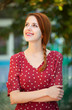 Redhead girl in red dress at outdoor near old house