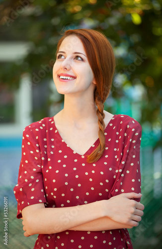 Photo: Redhead girl in red dress at outdoor near old house Redhead girl in red dress at outdoor near old house