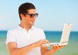 Handsome young man with laptop at beach background