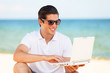 Handsome young man with laptop at beach background