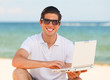 Handsome young man with laptop at beach background