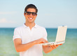 Handsome young man with laptop at beach background