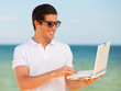 Handsome young man with laptop at beach background