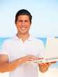 Handsome young man with laptop at beach background