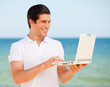 Handsome young man with laptop at beach background