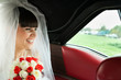 Bride laughing with bouquet of flowers inside red car