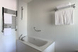 Bathtub, heated towel rail and shelf in bathroom.
