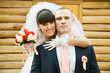 Bride hugging groom against blurred wooden house