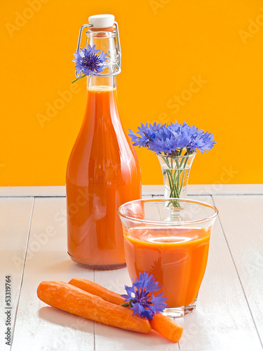 Photo: Möhrensaft im Glas und in einer Flasche auf einem Holztablett Möhrensaft im Glas und in einer Flasche auf einem Holztablett