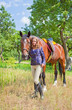 Young girl walking with a horse in the garden.