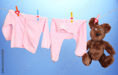 Photo: Baby clothes hanging on clothesline, on color background Baby clothes hanging on clothesline, on color background