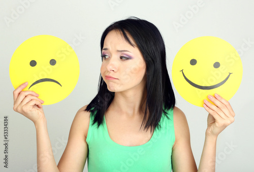 Photo: Young woman holding paper with sad and happy smiley Young woman holding paper with sad and happy smiley
