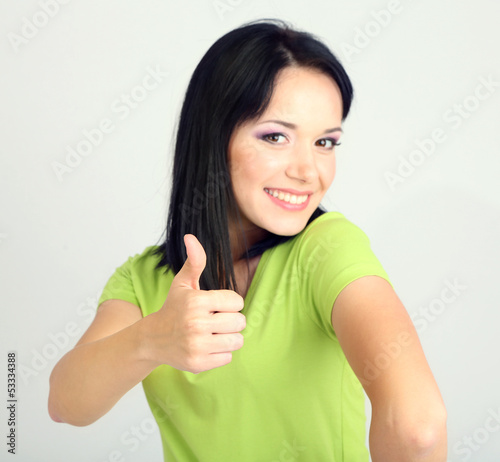 Photo: Happy young woman showing thumb up sign on grey background Happy young woman showing thumb up sign on grey background