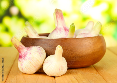 Photo: Fresh garlic in bowl, on wooden table, on bright background Fresh garlic in bowl, on wooden table, on bright background