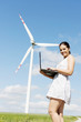 Teen girl with laptop next to wind turbine.
