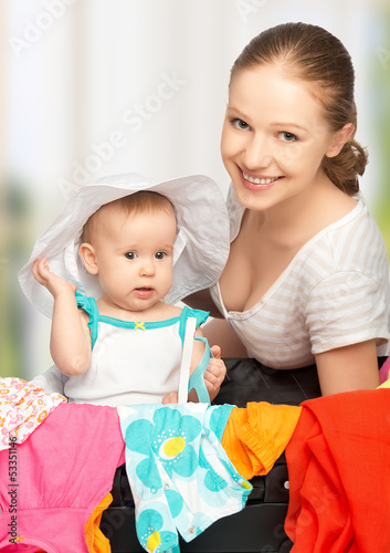 Photo: mother and baby girl with suitcase and clothes ready for traveli mother and baby girl with suitcase and clothes ready for traveli